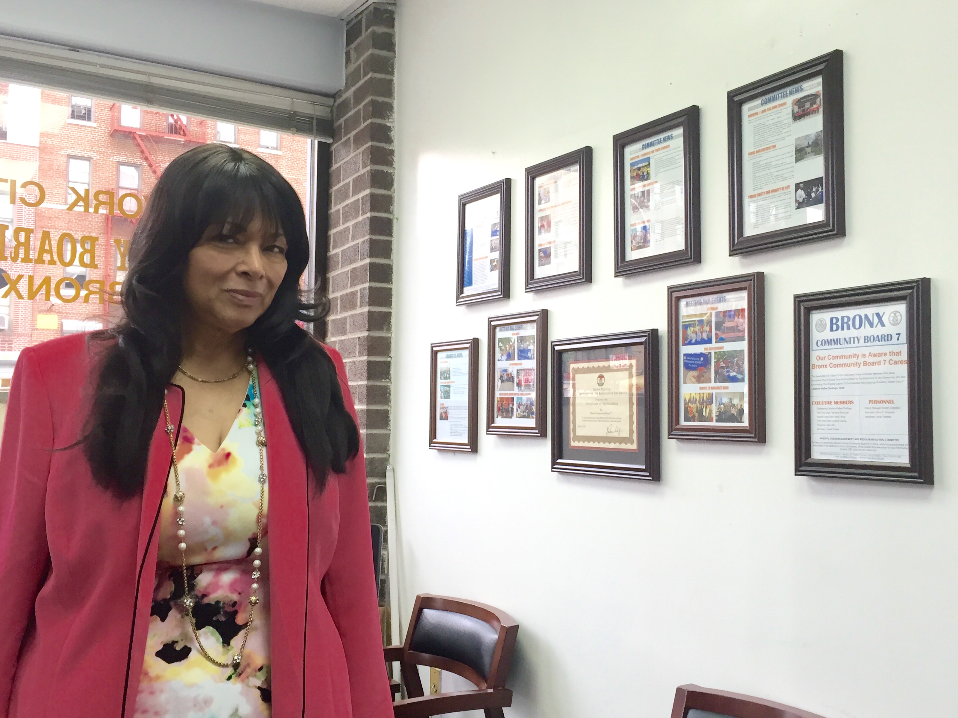 ADALINE WALKER-SANTIAGO, chair of Community Board 7, stands alongside individually framed pages of the latest CB7 newsletter.