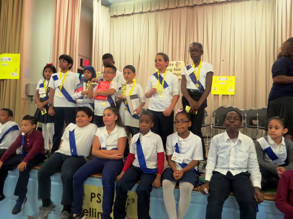 W-I-N-N-E-R-S! This year’s PS 94 spelling bee champs are (top row, 3rd, 4th and 5th from left), Nadia Sharia, Brian Puma, and Abdullah Zidan, each holding a golden trophy. They’re joined by other participating spelling bee students.  Photo by Michael Brown Jr.  